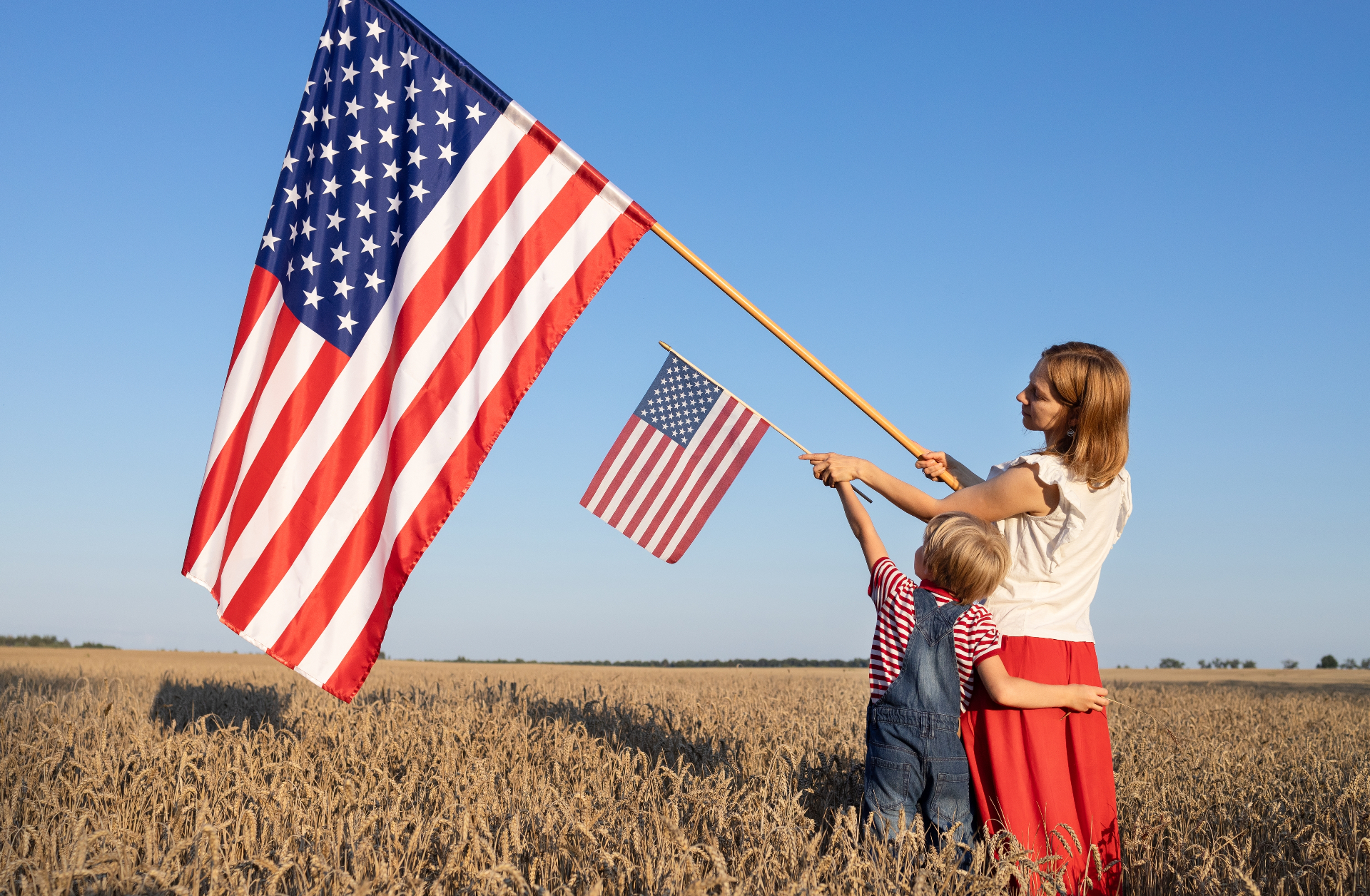 Mother and child holding American flags in a wheat field